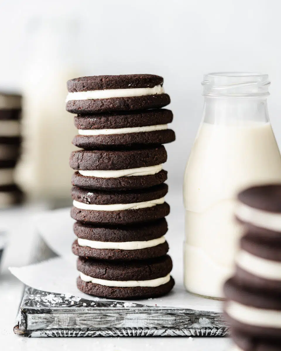 stack of homemade vegan oreo cookies with a bottle of milk next to them.