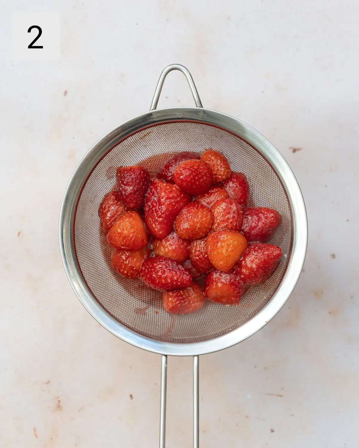 cooked strawberries on a fine-mesh sieve.