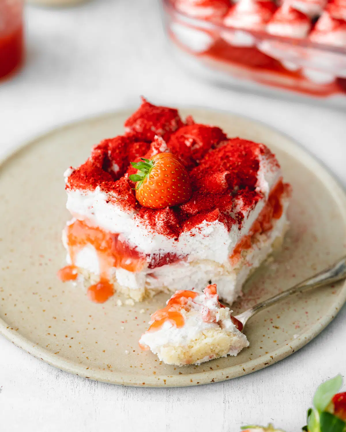 layered strawberry tiramisu on a plate with fresh strawberries and strawberry sauce.