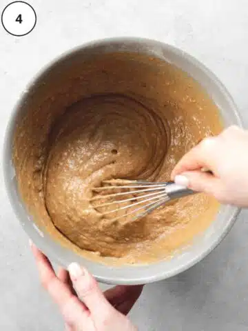 whisking carrot cake batter with a whisk in a large bowl.
