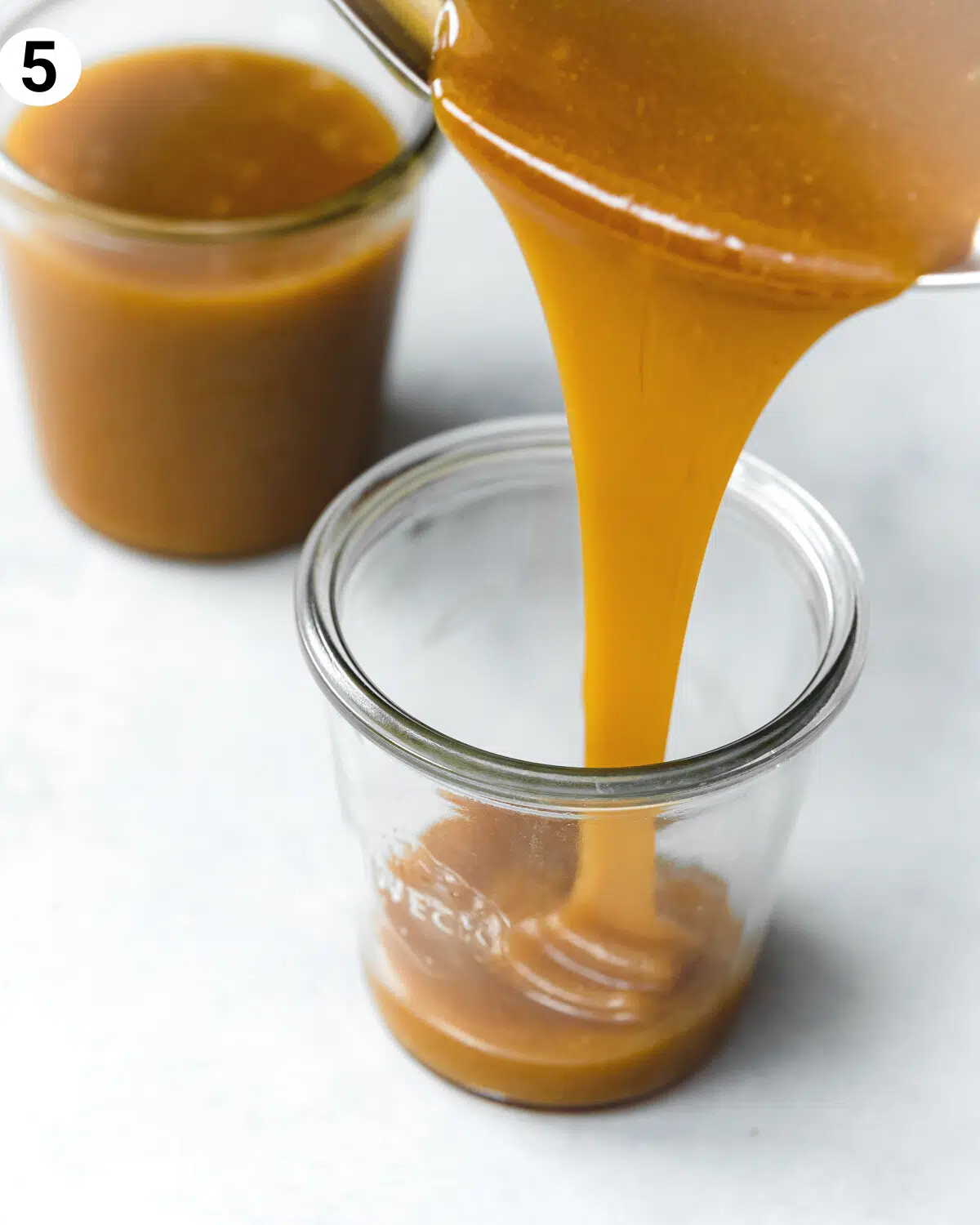pouring caramel sauce into a glass jar.