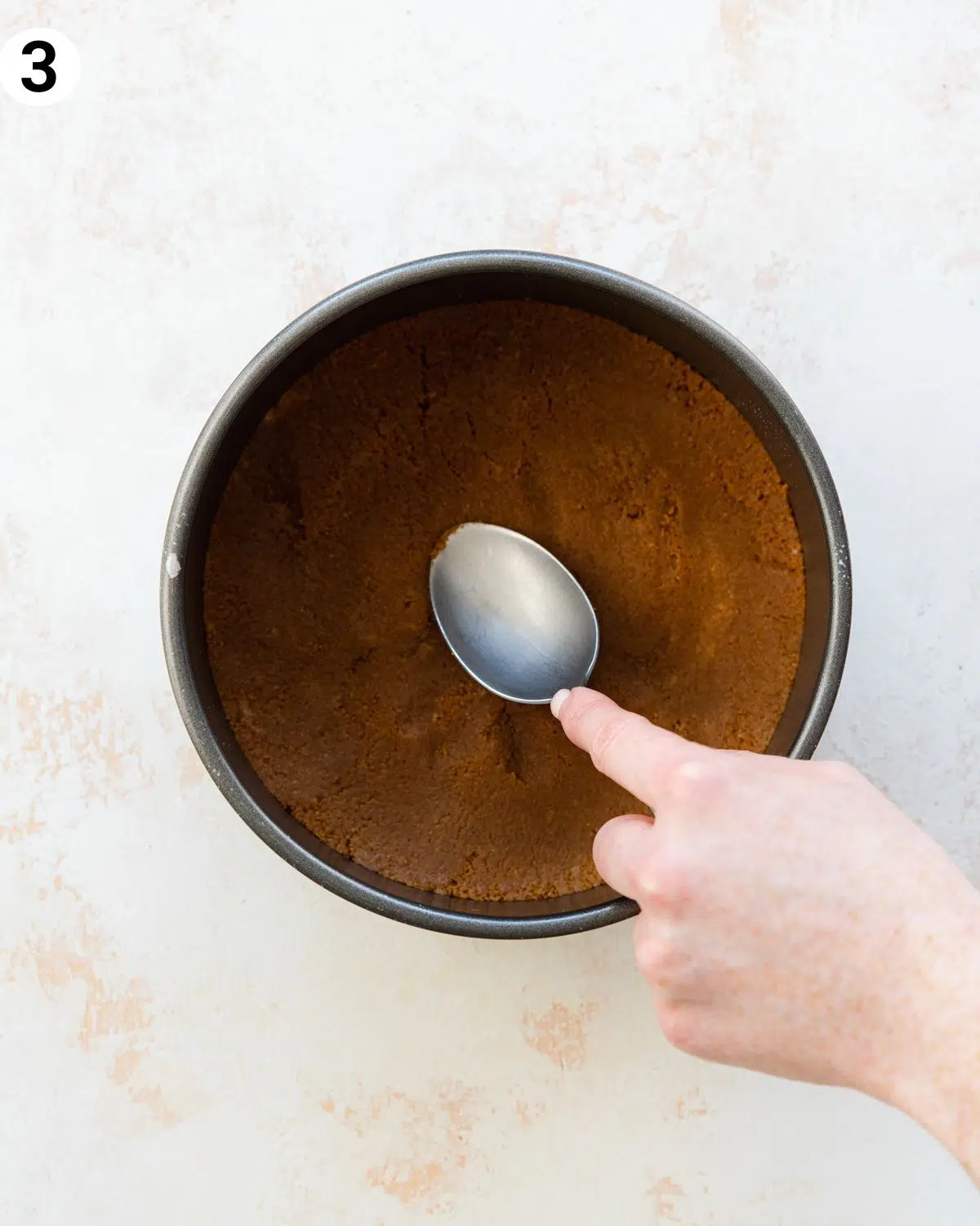 press biscoff cookie base into a cake tin with a spoon.
