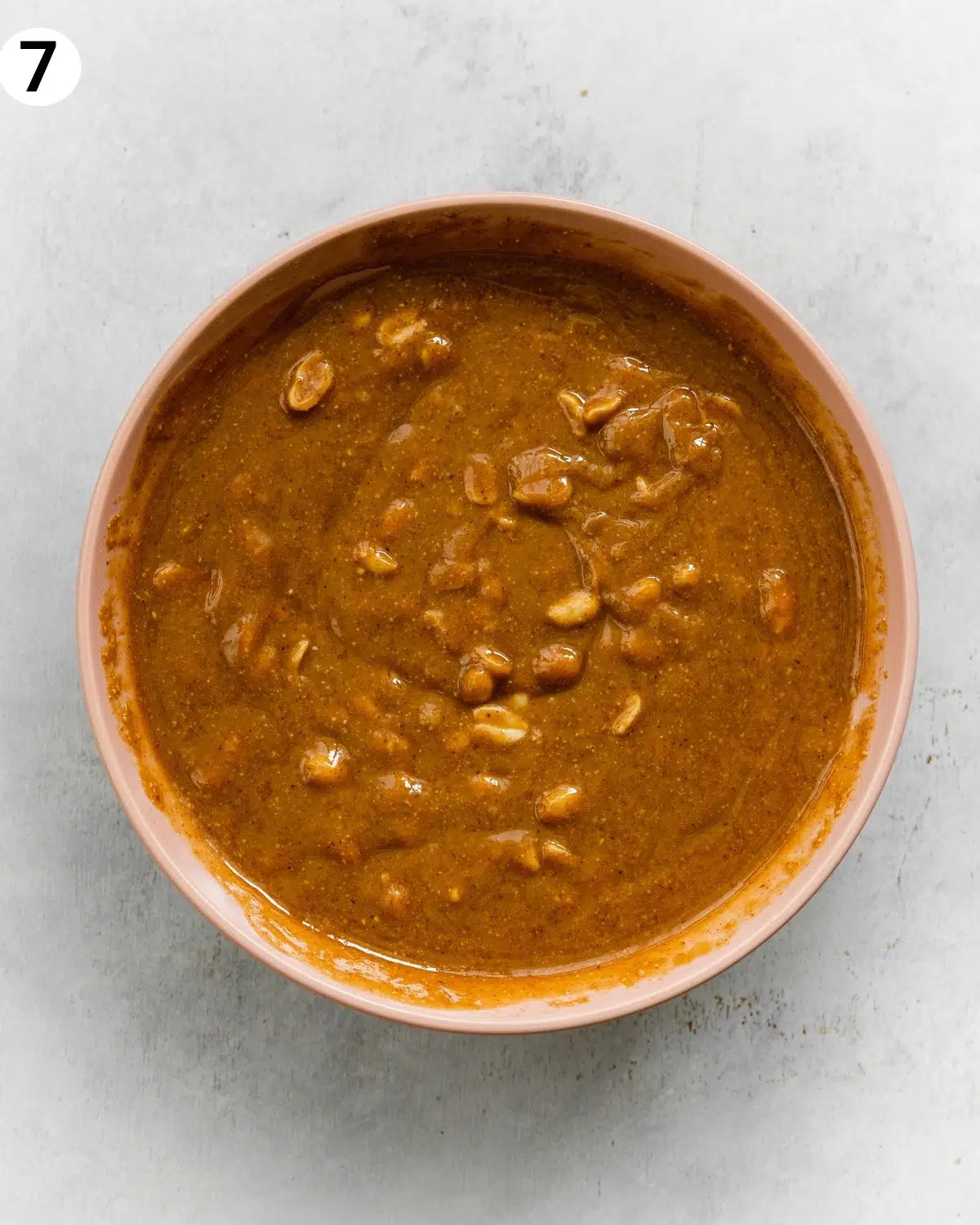top down view of peanut butter caramel with peanuts in a pink bowl on top of a grey surface.
