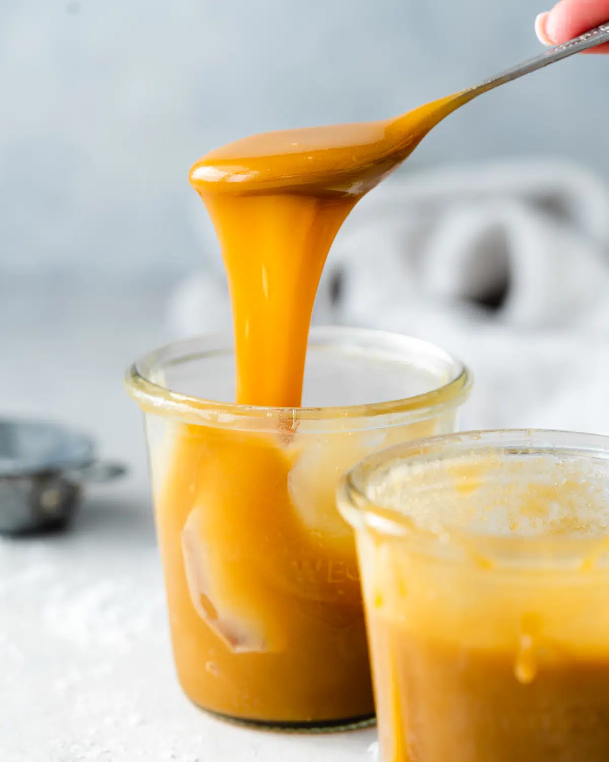 side view of two jars of caramel sauce with a spoon lifting some out of one of the jars.