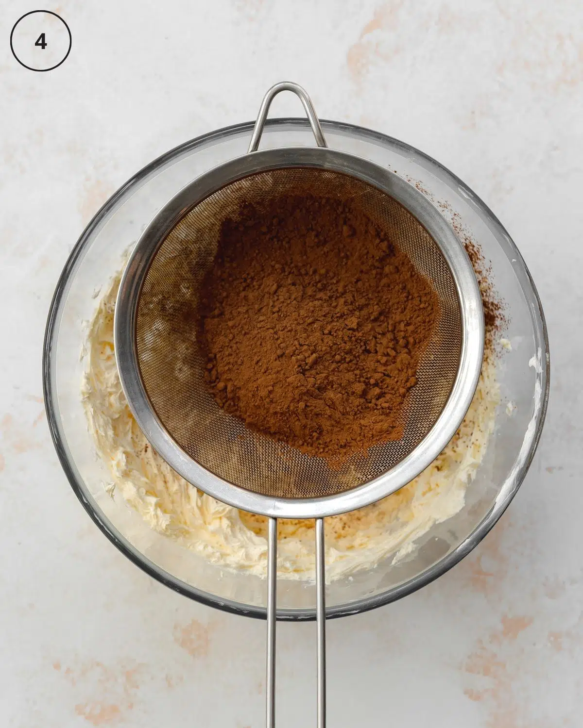 sieve with cocoa powder sitting on top of a glass bowl.