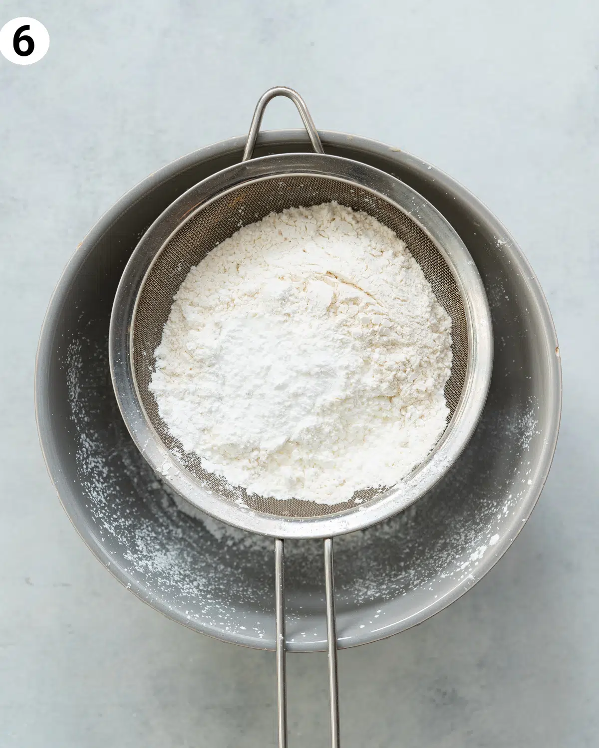 flour in a sieve sitting on top of a bowl.