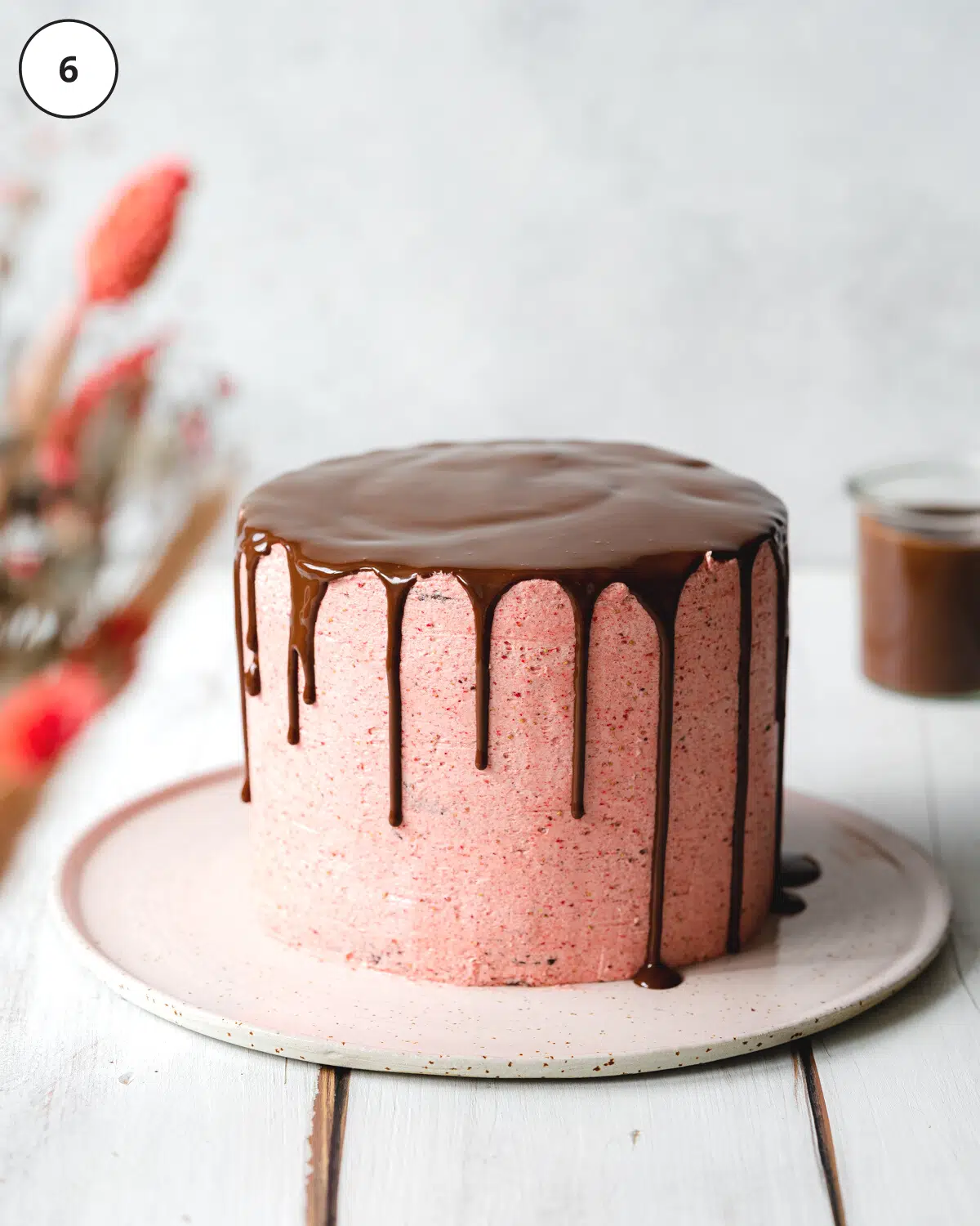 pink cake with chocolate ganache drip on a ceramic plate.