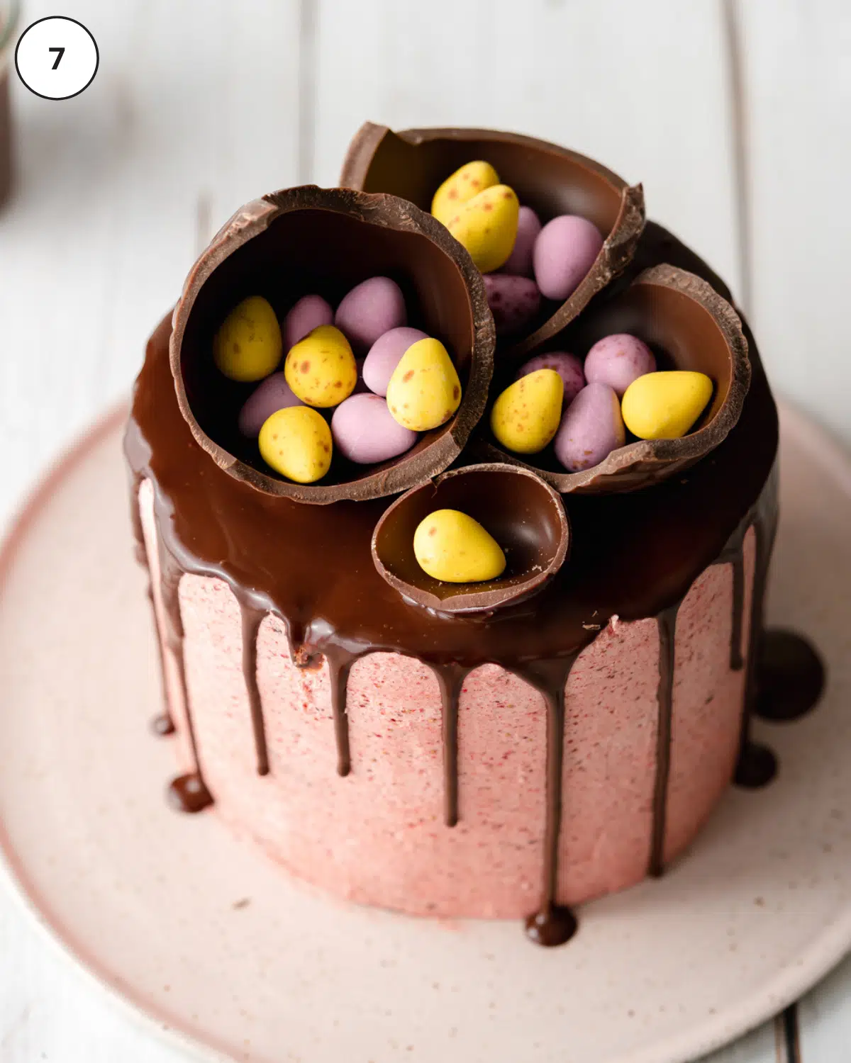 pink cake with chocolate ganache drip on a ceramic plate with easter eggs on top.