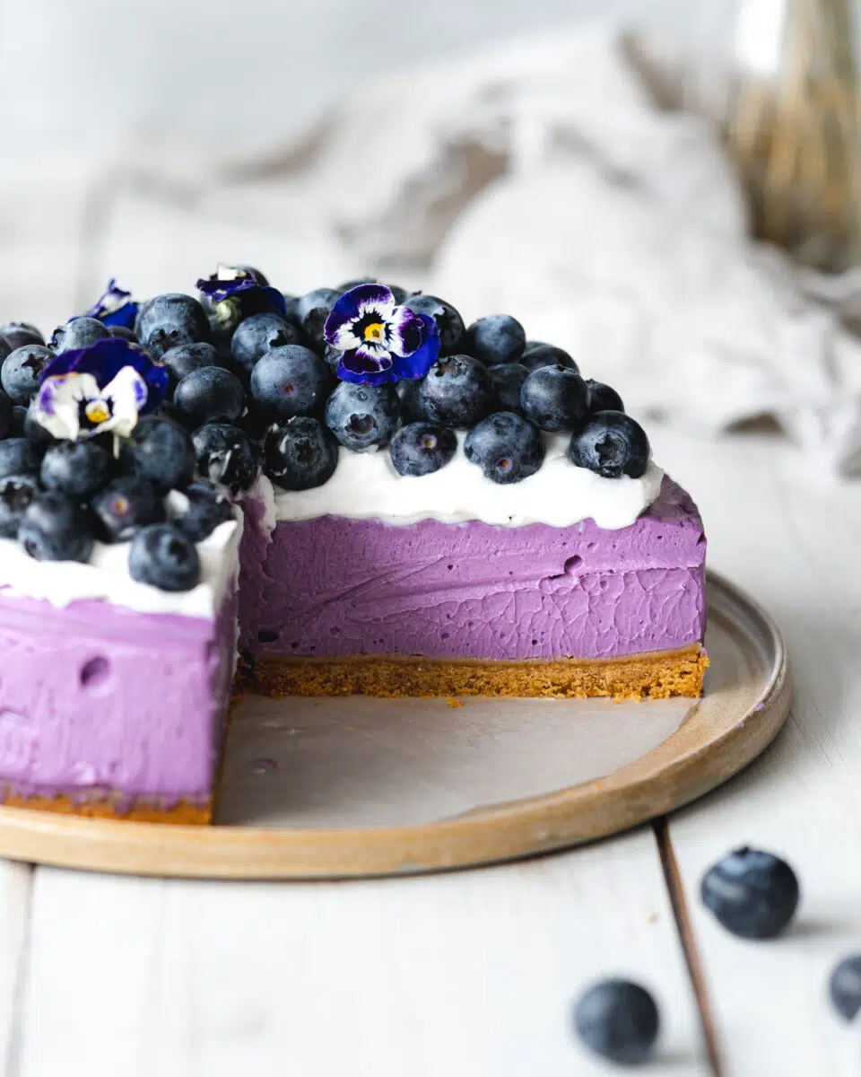 side view of blueberry cheesecake with fresh blueberries on top on a ceramic plate.