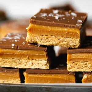 stack of chocolate peanut butter slices with an oaty base and sea salt sprinkled on top.