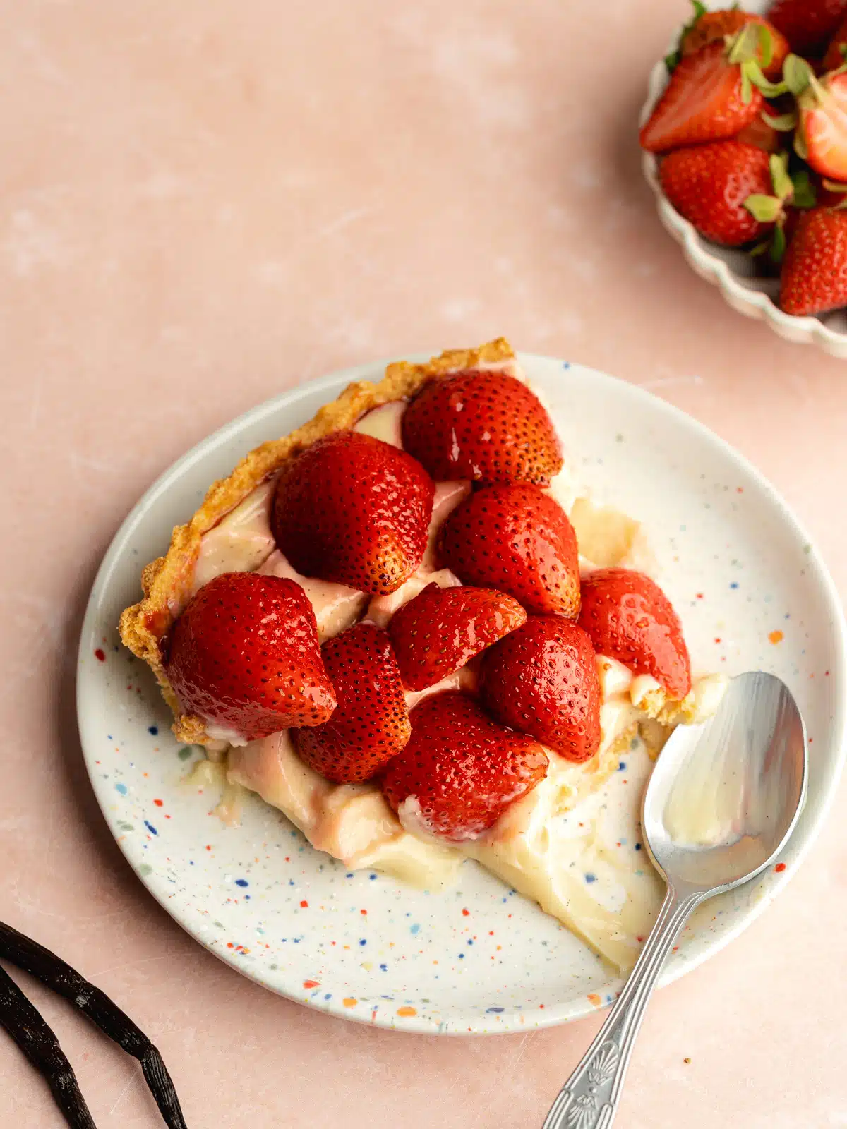 a slice of strawberry custard tart on a ceramic plate with a bitefull taken from it.