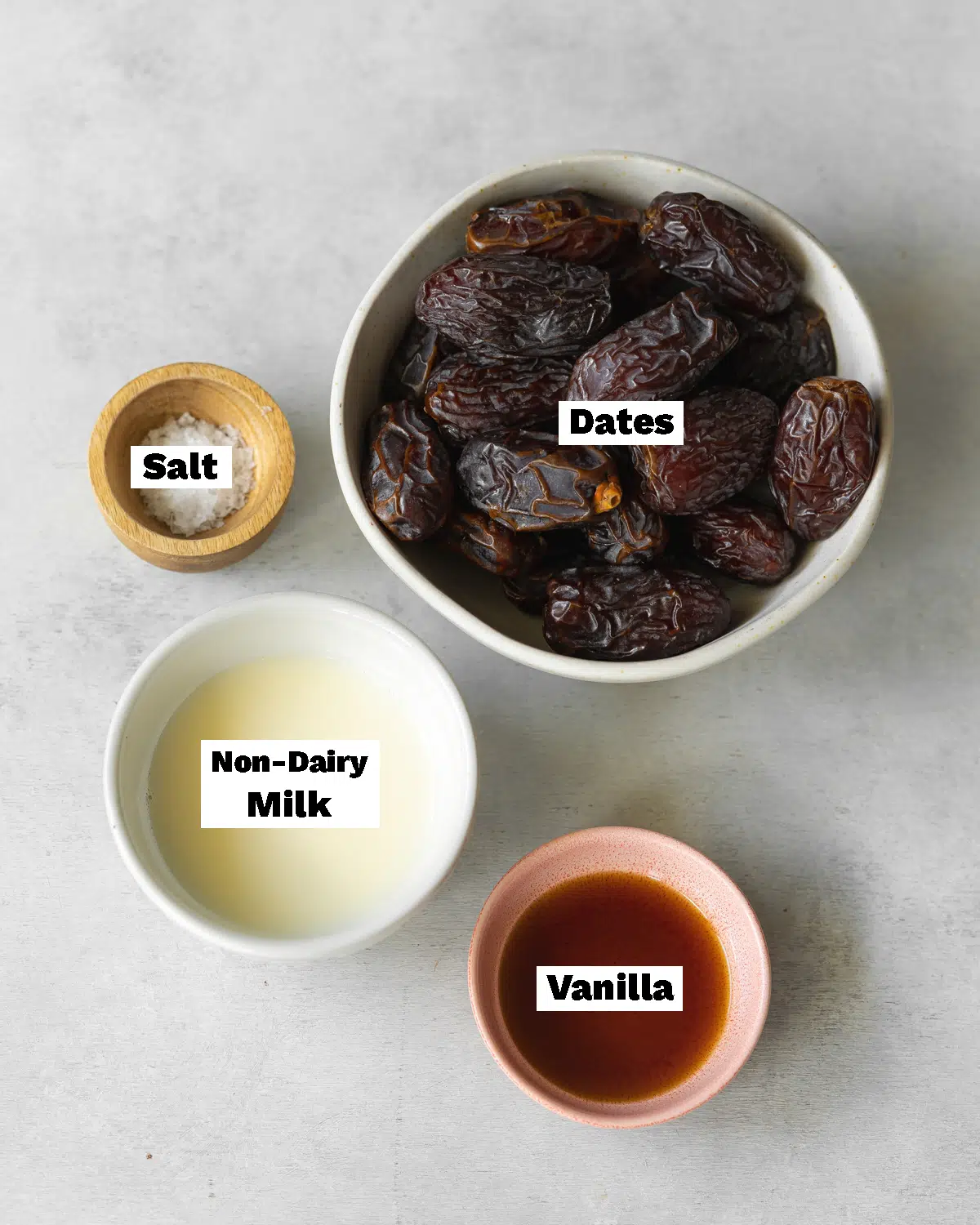 ingredients for making vegan date caramel measured out in bowls on a grey surface.