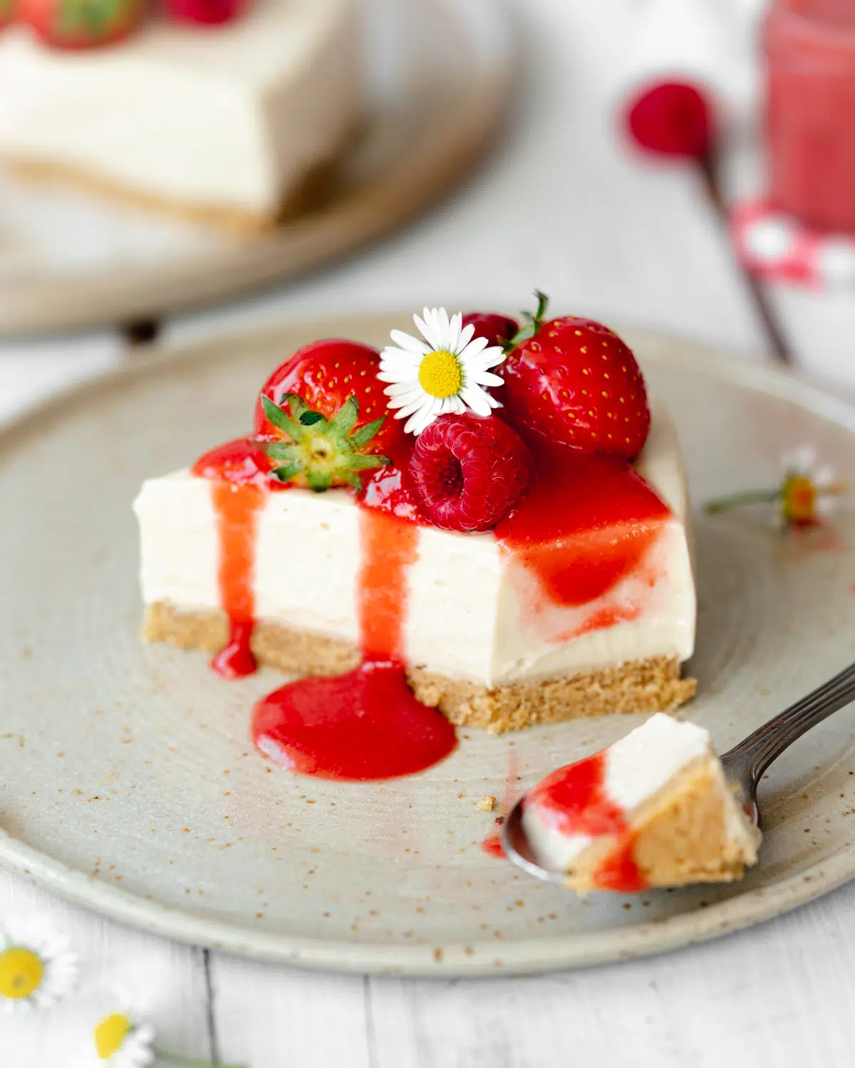 slice of no bake vegan cheesecake on a plate topped with fresh berries and strawberry sauce.