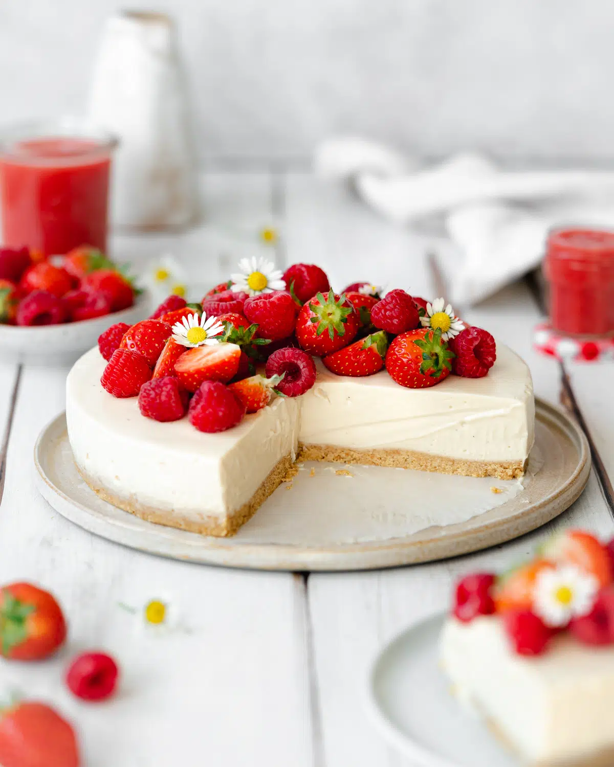 no bake cheesecake with fresh berries and flowers on top on a white wooden surface.