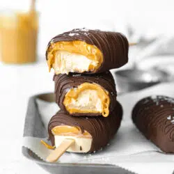 peanut butter ice cream bars coated in chocolate stacked on a metal tray with parchment paper.