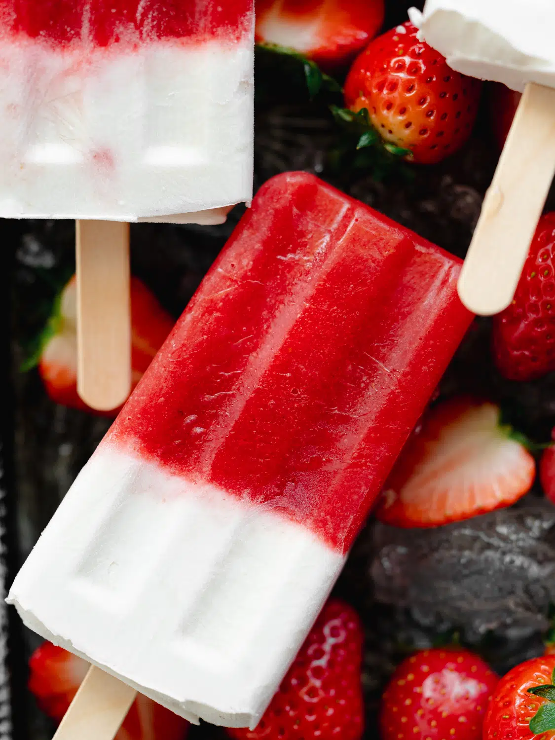 strawberry cream popsicles on a tray with ice and berries.