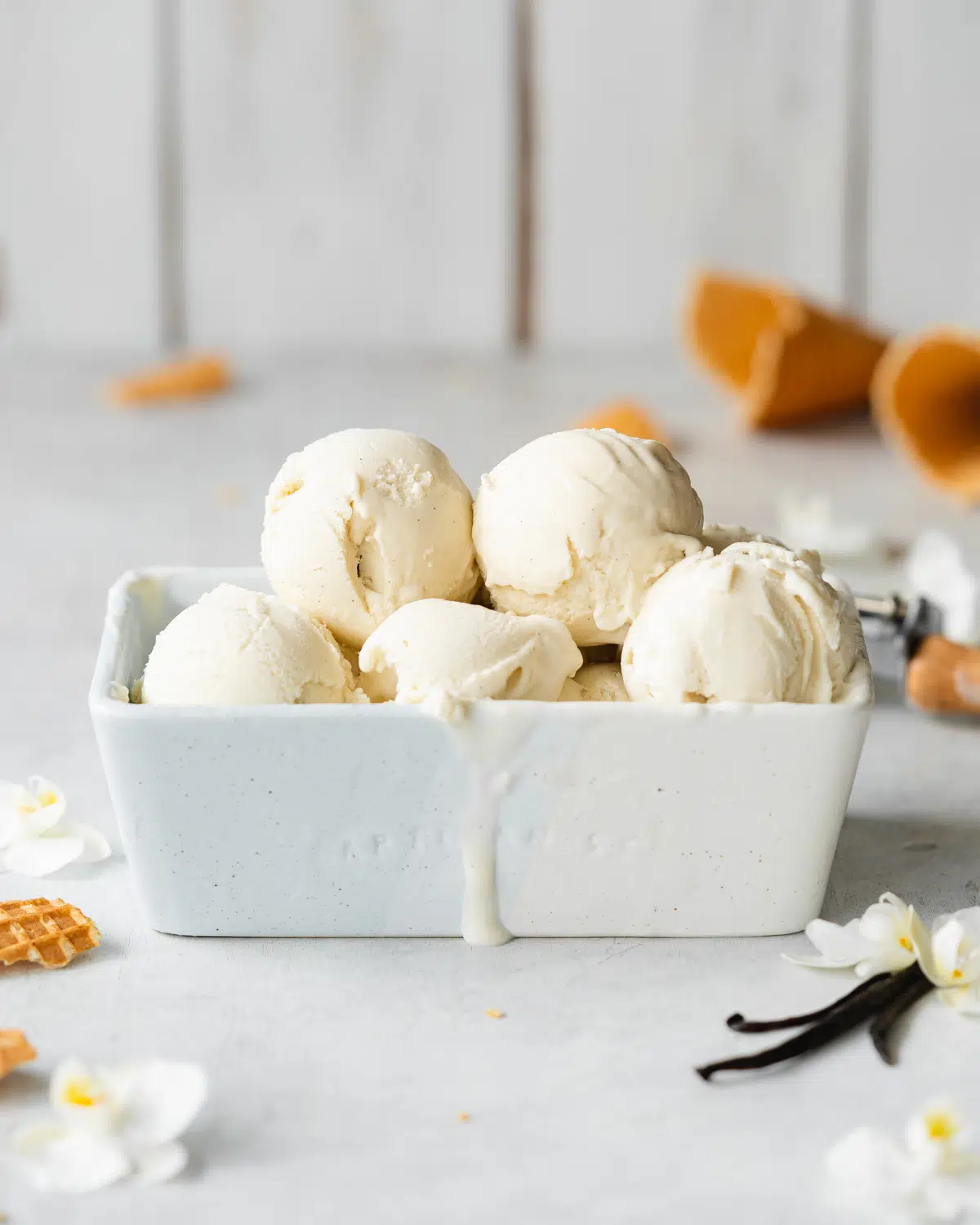 vegan vanilla ice cream scoops with vanilla pods and vanilla flowers in a powder blue ceramic dish.