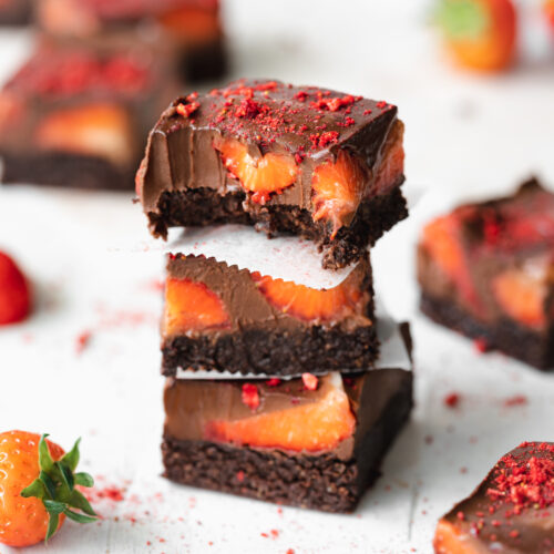stack of strawberry brownies with fresh strawberries scattered around them.