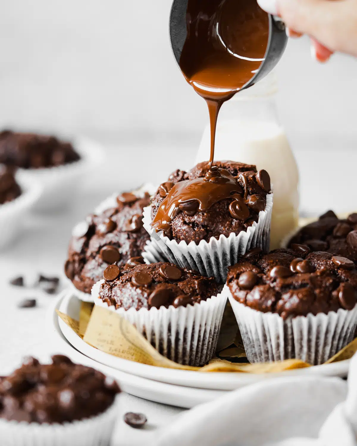 pouring melted chocolate over a stack of vegan chocolate muffins.