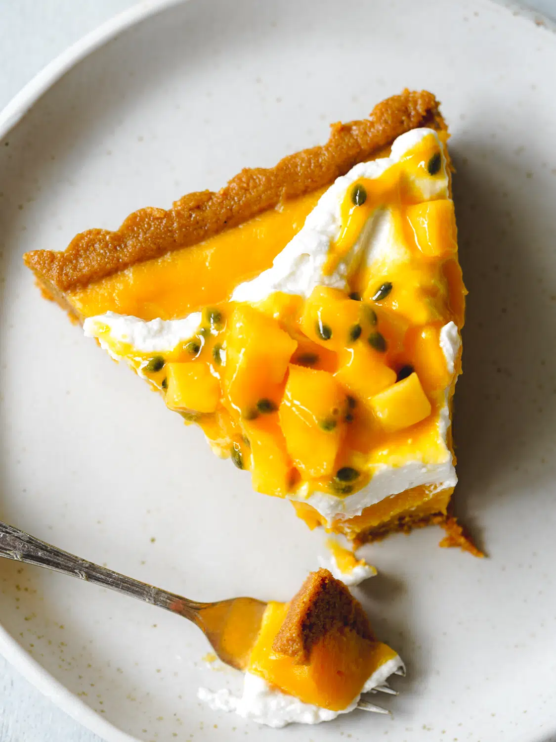 slice of mango tart on a plate with mango chunks, passion fruit coulis, and coconut cream.