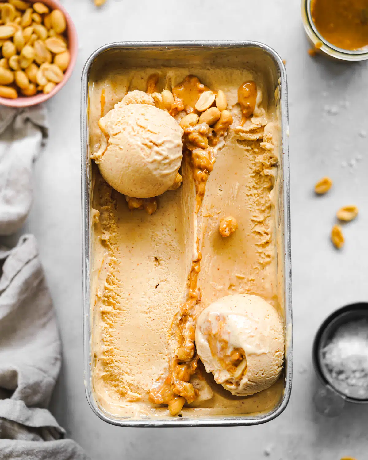 peanut butter ice cream in a loaf pan with roasted peanuts scattered around it.