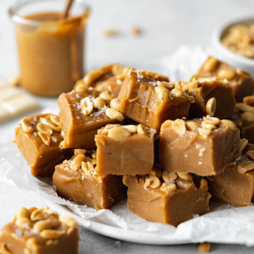 stack of peanut butter fudge on a plate with peanut butter in the background.