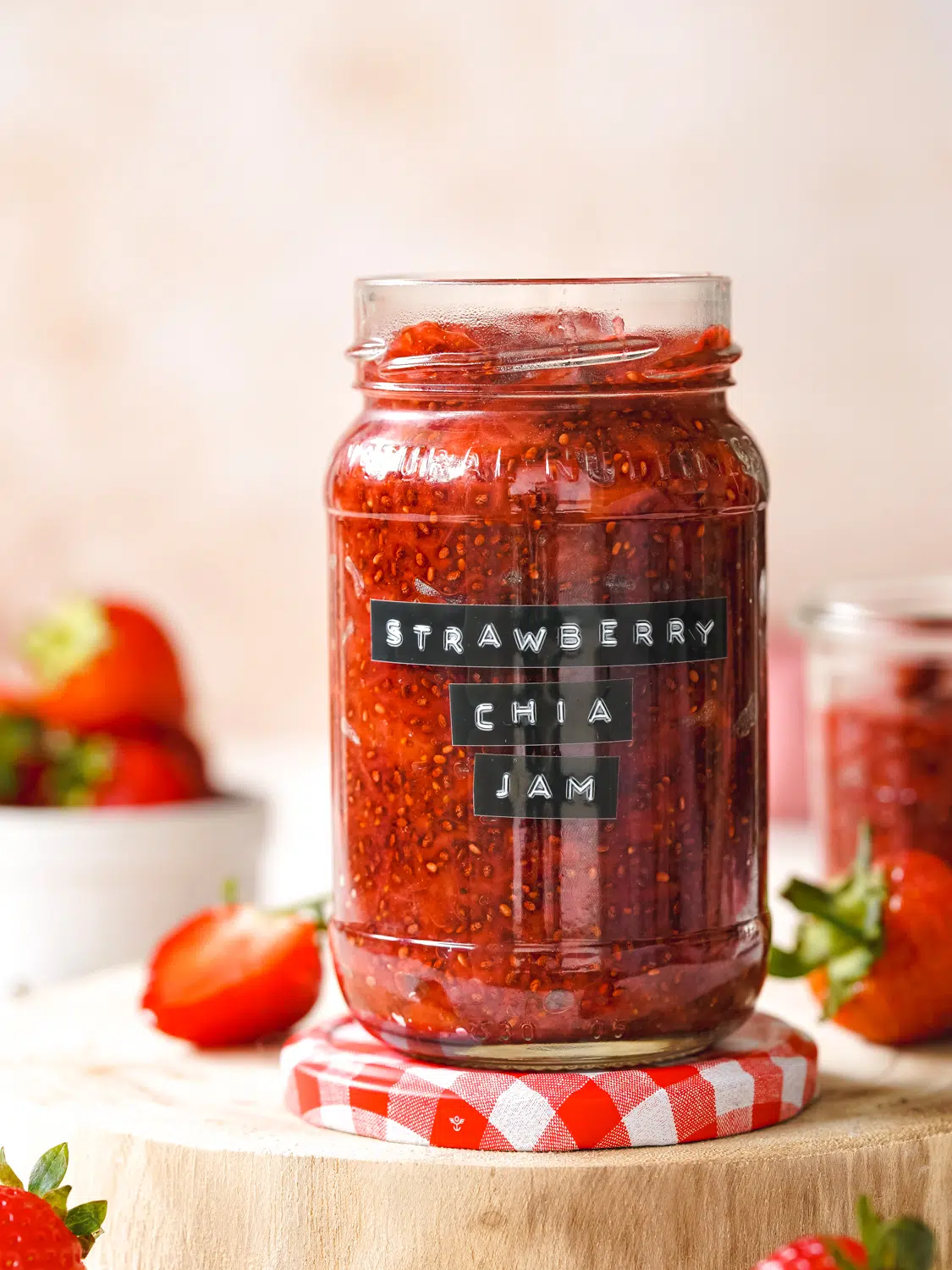 jar of strawberry jam with fresh strawberries scattered around it.