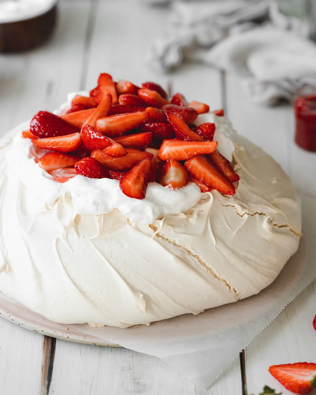 vegan pavlova with fresh strawberries and cream on a white wooden surface.