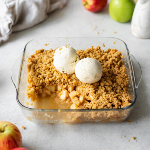 apple crumble in a baking dish with scoops of vanilla ice cream on top.