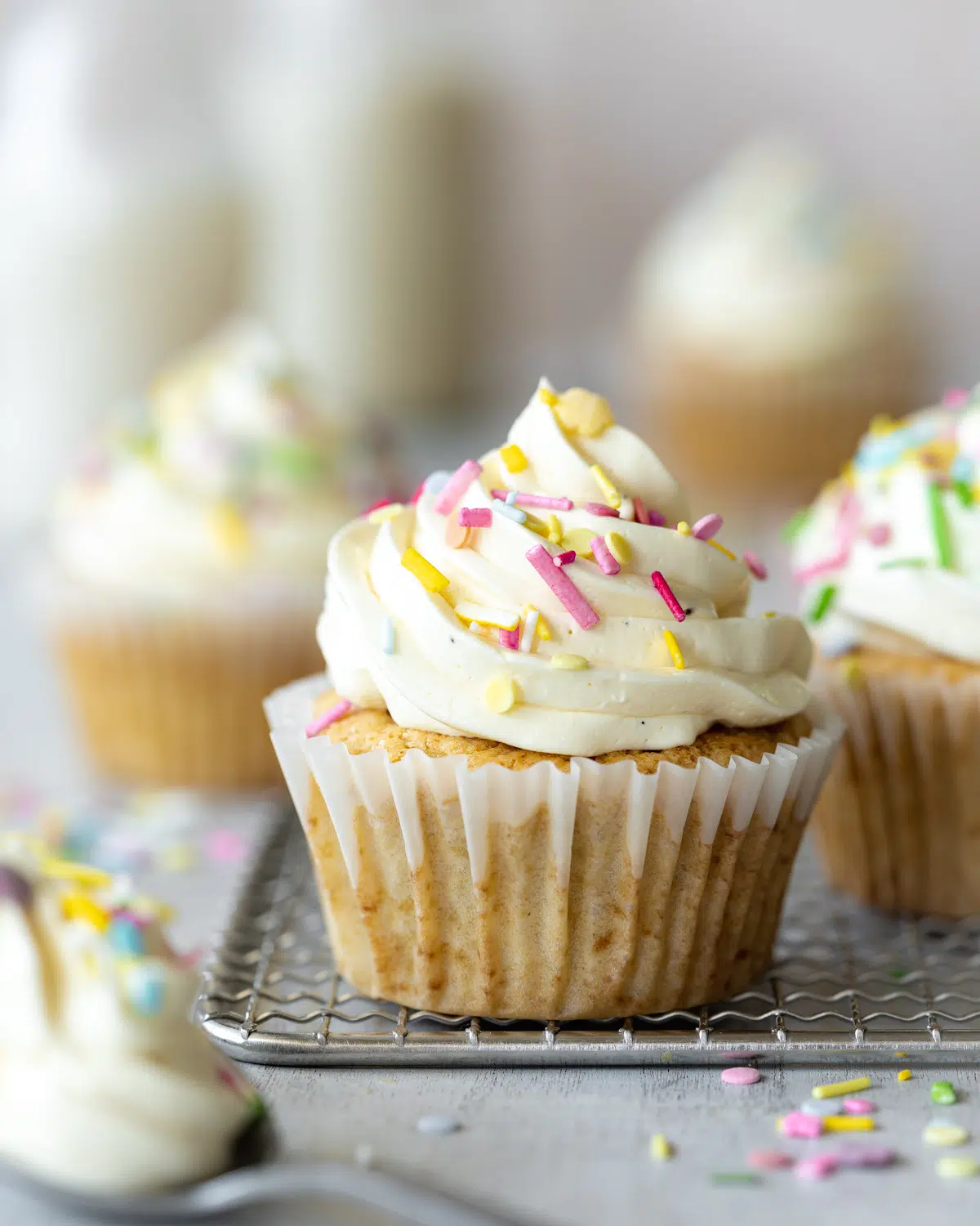 vanilla cupcakes with funfetti spinkles and frosting on a cooling rack.