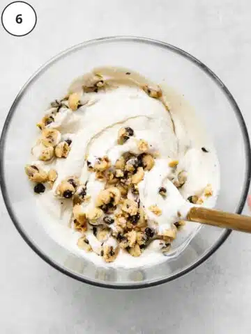 vegan vanilla ice cream softened in a large bowl with cookie dough chunks being mixed throughout.