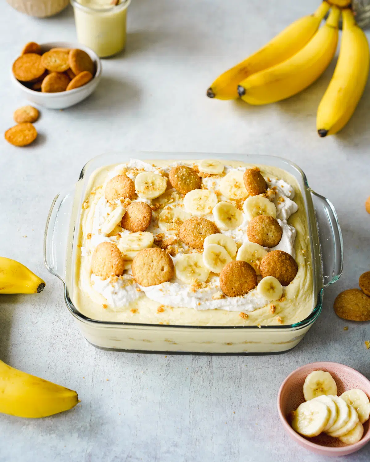 fresh banana pudding in a baking dish with bananas and vanilla wafers scattered around it.