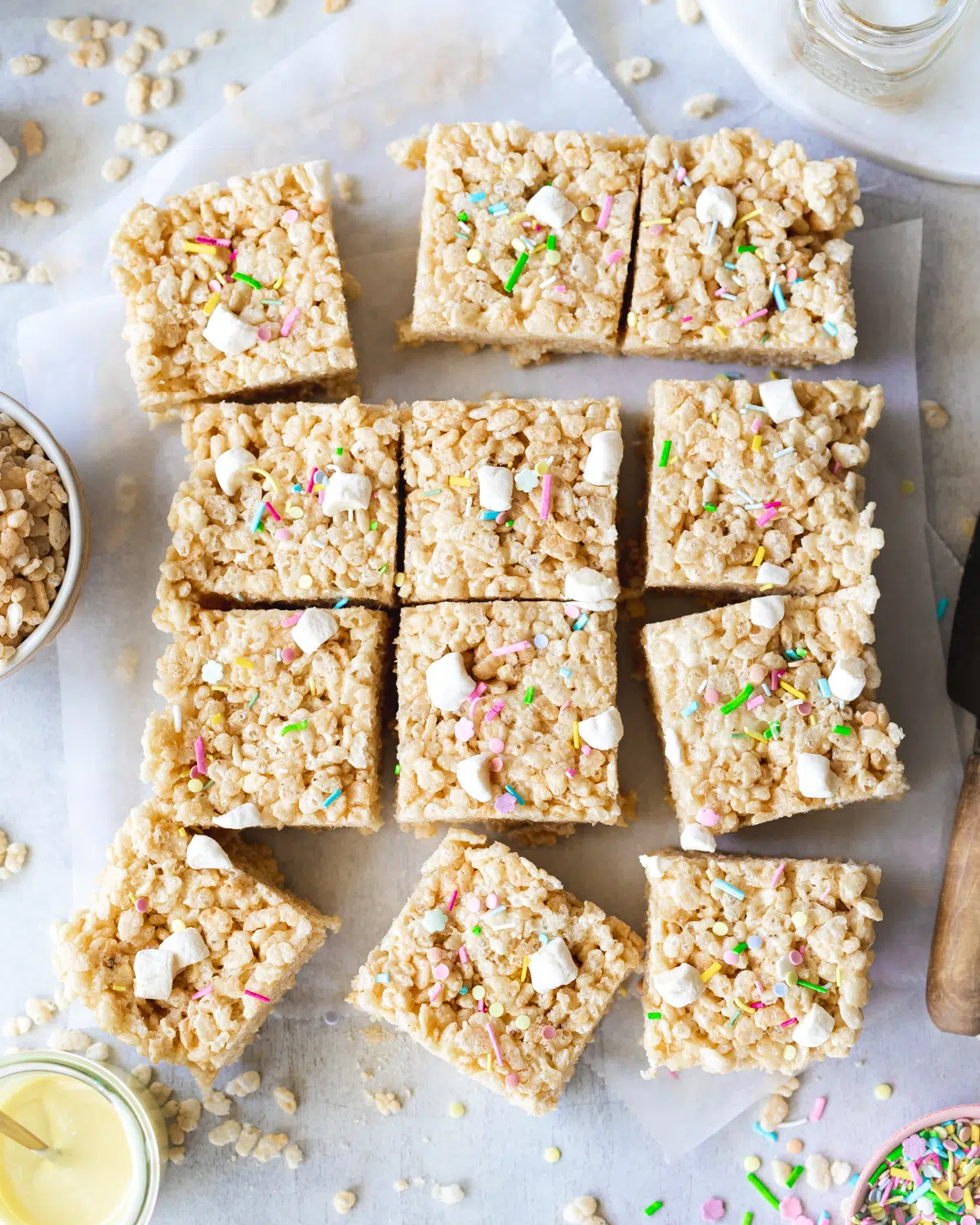 vegan rice crispy treats on parchment paper topped with mini marshmallows and funfetti.