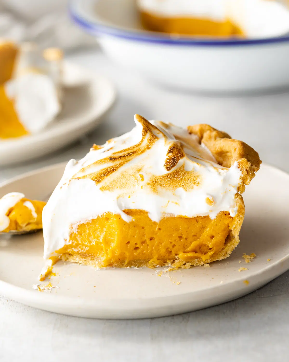 slice of sweet potato pie with meringue topping on a plate with a bite taken from it.