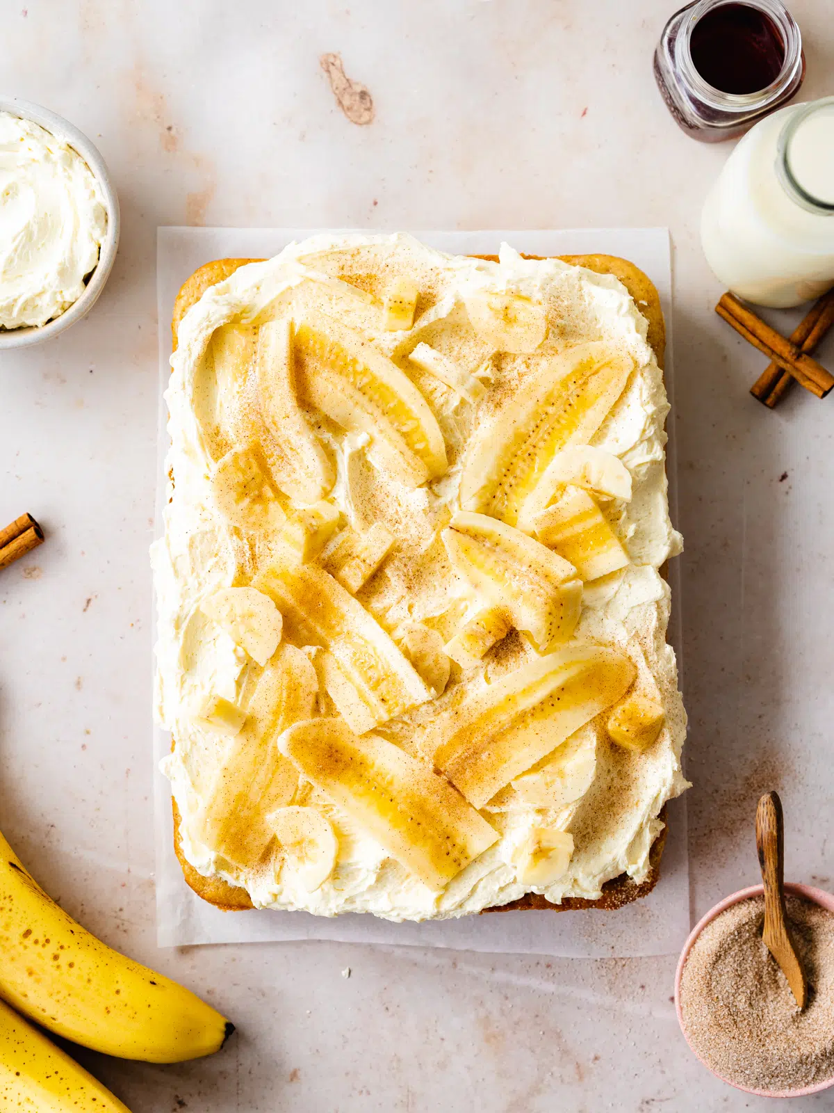 banana sheet cake with cream cheese frosting and banana slices on a peach surface.
