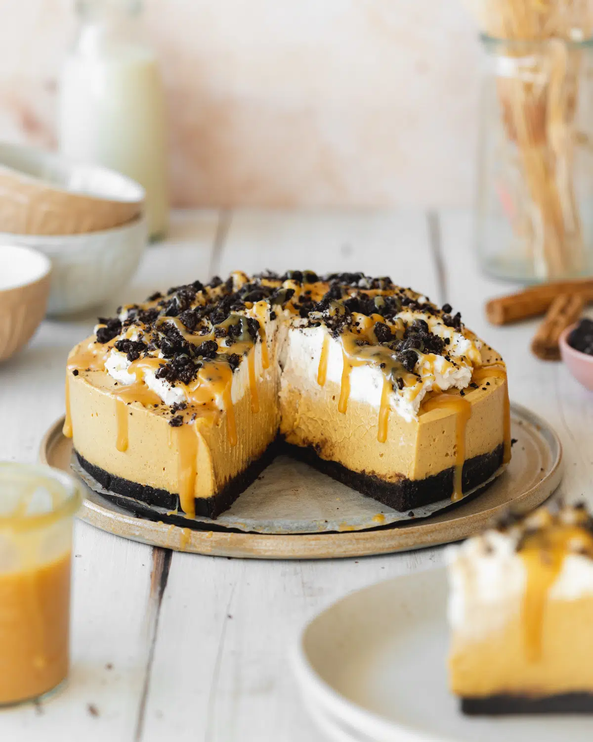 pumpkin cheesecake with oreo crust on a ceramic plate with caramel sauce and coconut cream on top.