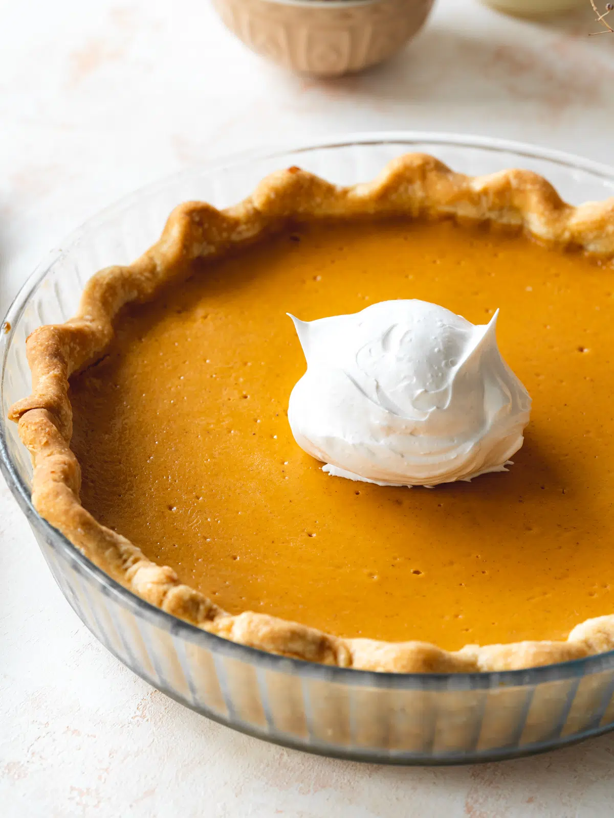 sweet potato pie with a scoop of Italian meringue on top in a clear pie dish.