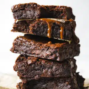 stack of fudgy brownies with chocolate sauce dripping down the sides.