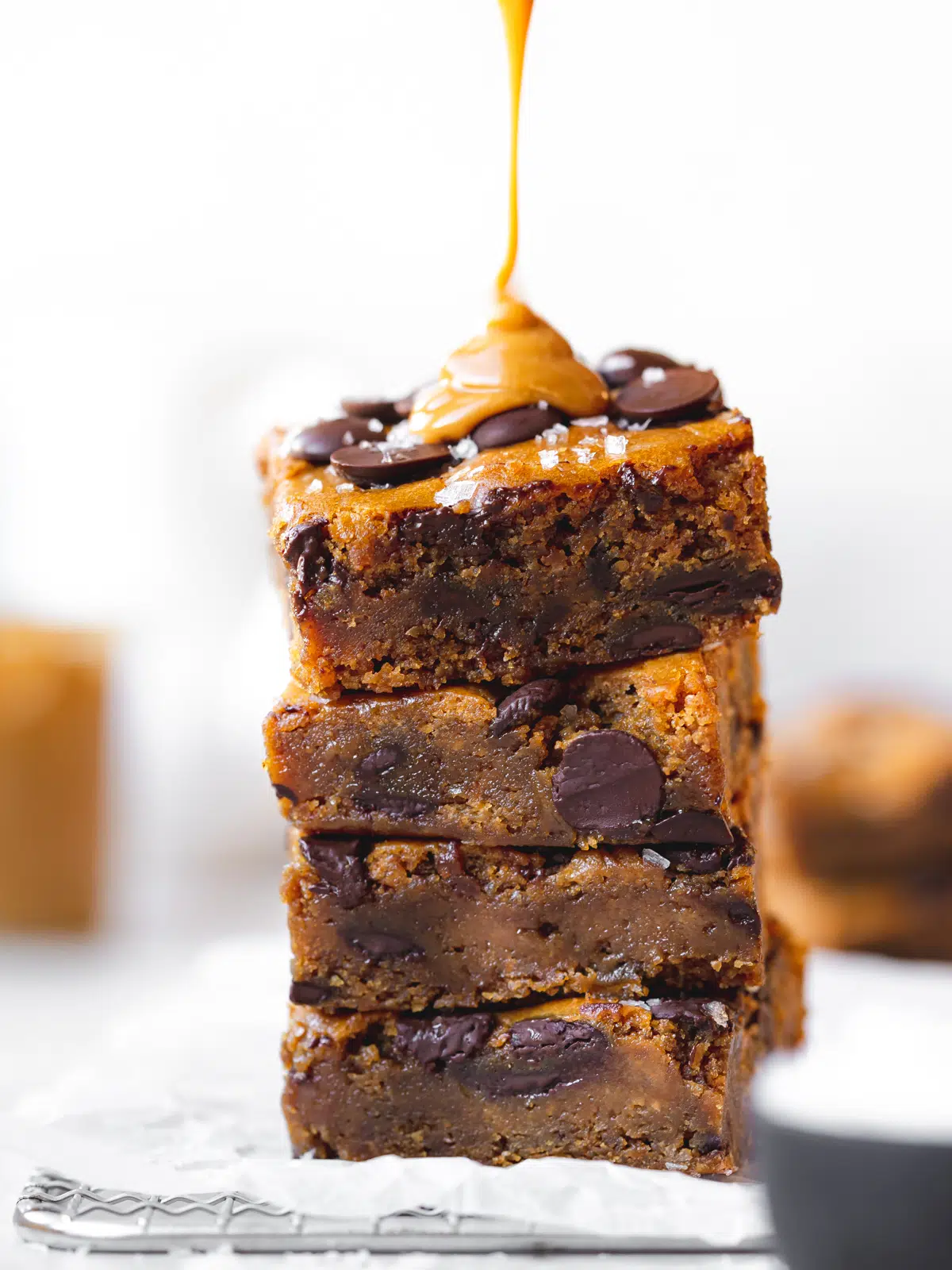 a stack of chocolate chip blondies with peanut butter being drizzled on top.