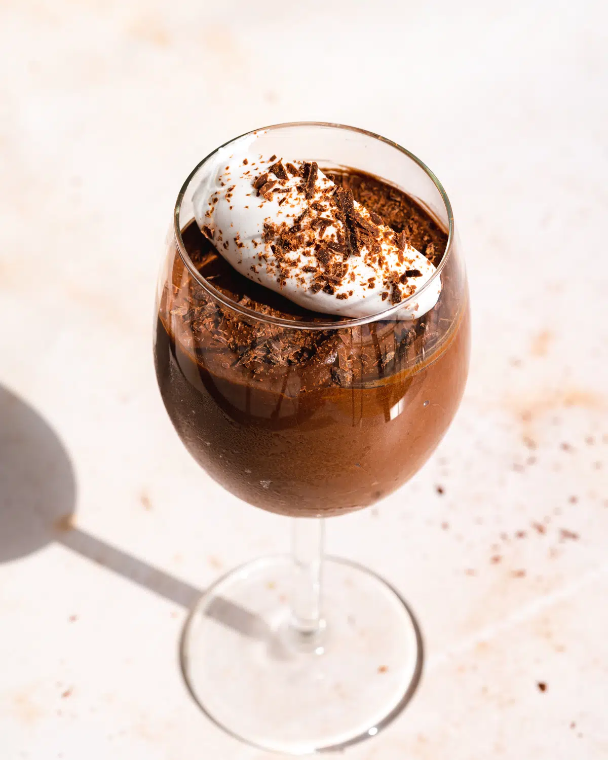 a wine glass with chocolate mousse and whipped cream with direct sunlight shining on it.