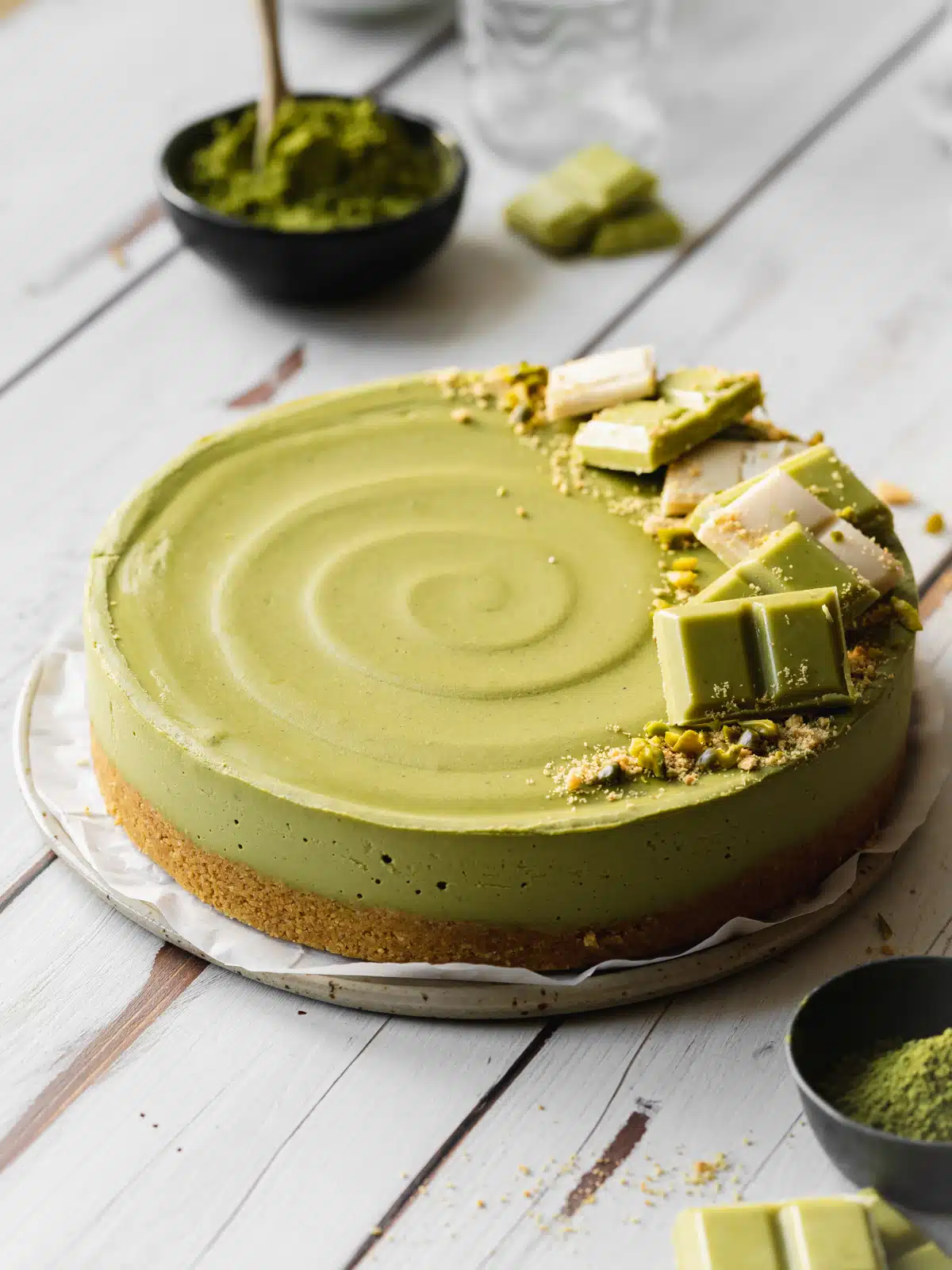 matcha cheesecake with white chocolate on top on a white wooden surface.