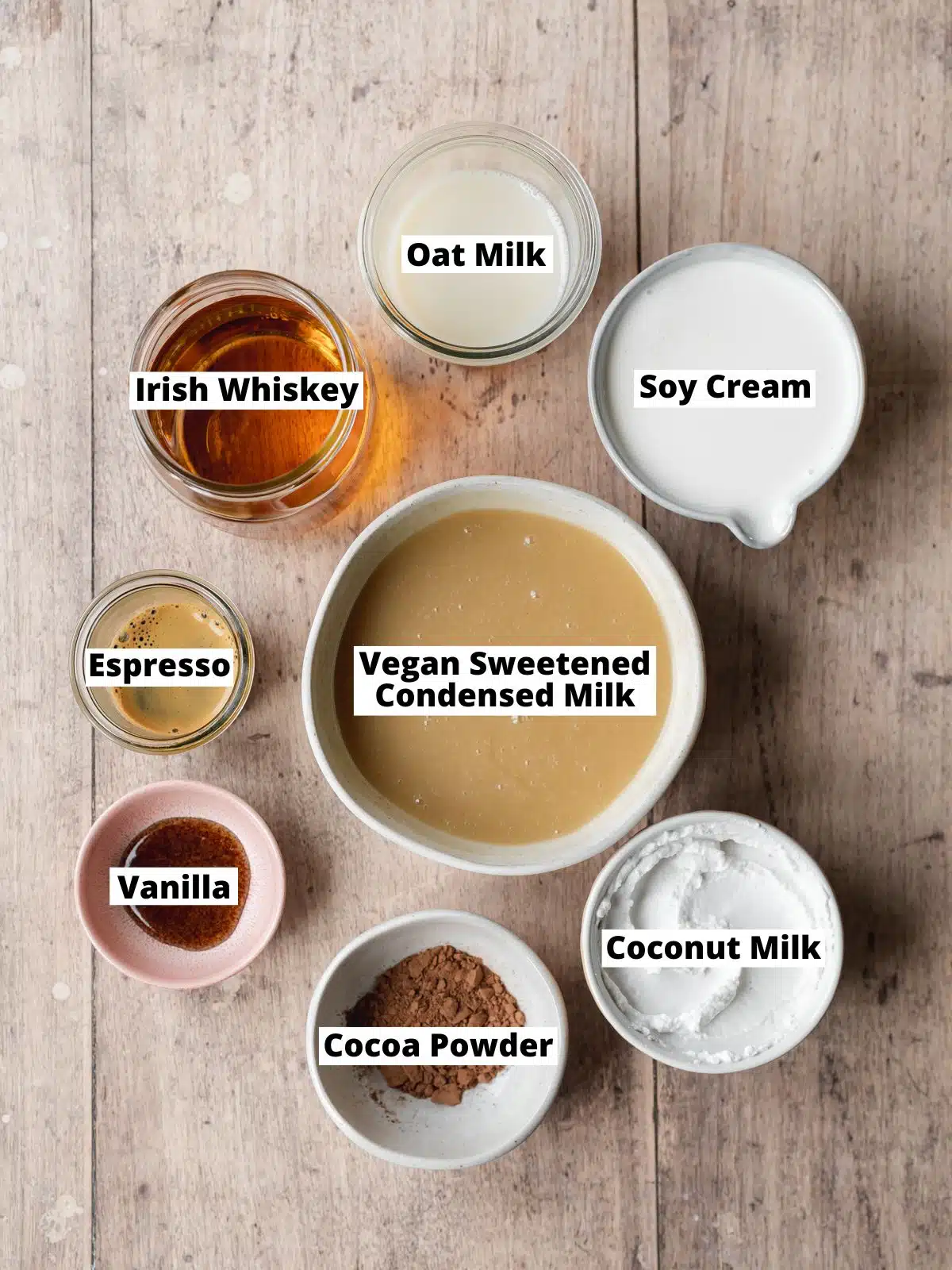 ingredients for vegan baileys measured out in bowls on a wooden table.
