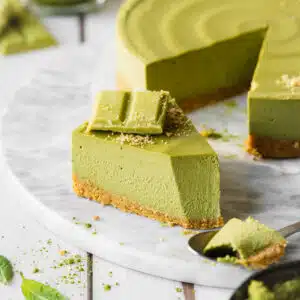 slice of matcha cheesecake on a marble slab next to a full cheesecake.