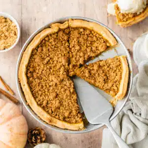 pumpkin pie with crumble topping on a wooden surface with pumpkins next to it.