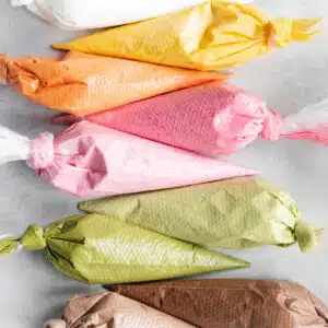 pink, green, yellow, orange, brown and white royal icing in piping bags.