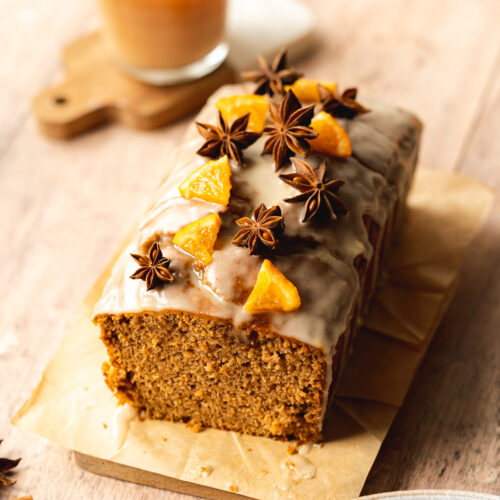 a loaf of sweet chai bread with orange segments, star anise, and icing on top of a wooden board.