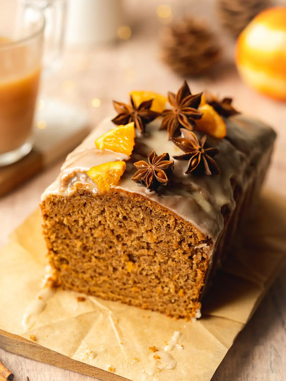 a loaf of sweet chai bread with orange segments, star anise, and icing on top of a wooden board.