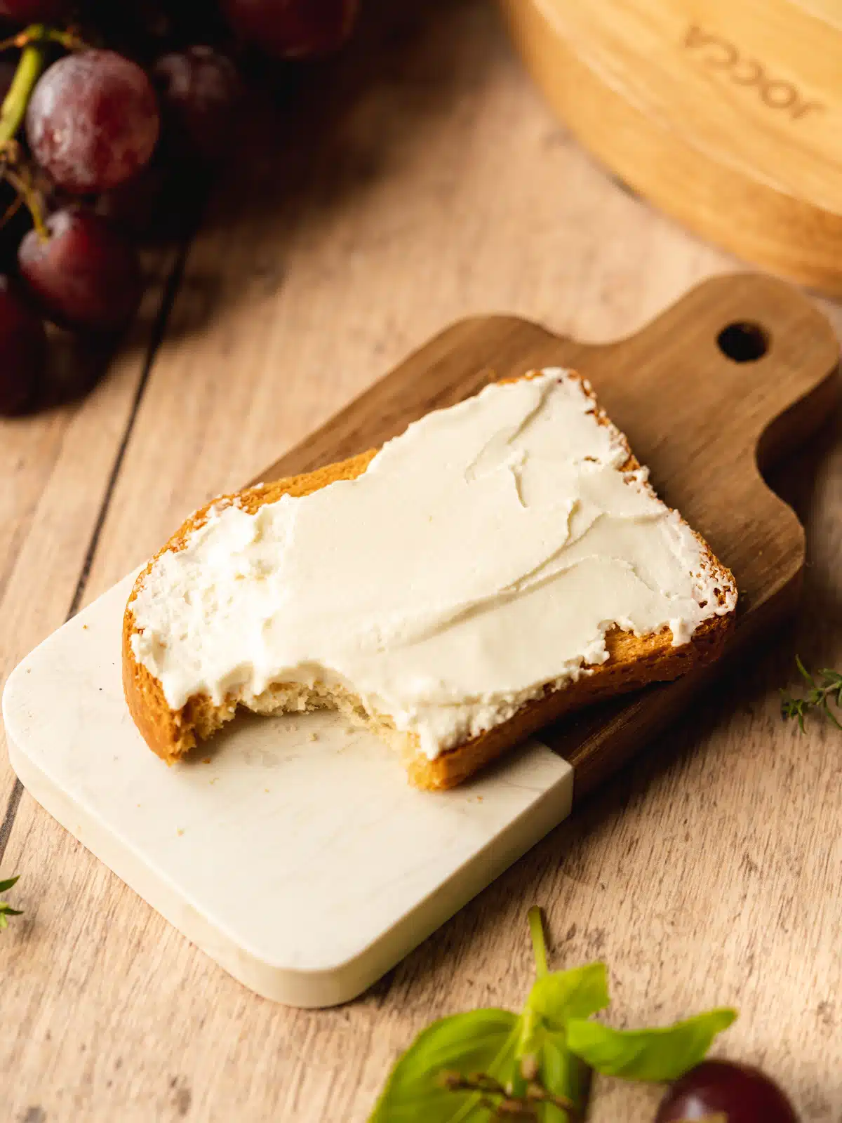 slice of toast topped with a smear of homemade vegan cream cheese on a two-toned cutting board with a wooden handle.