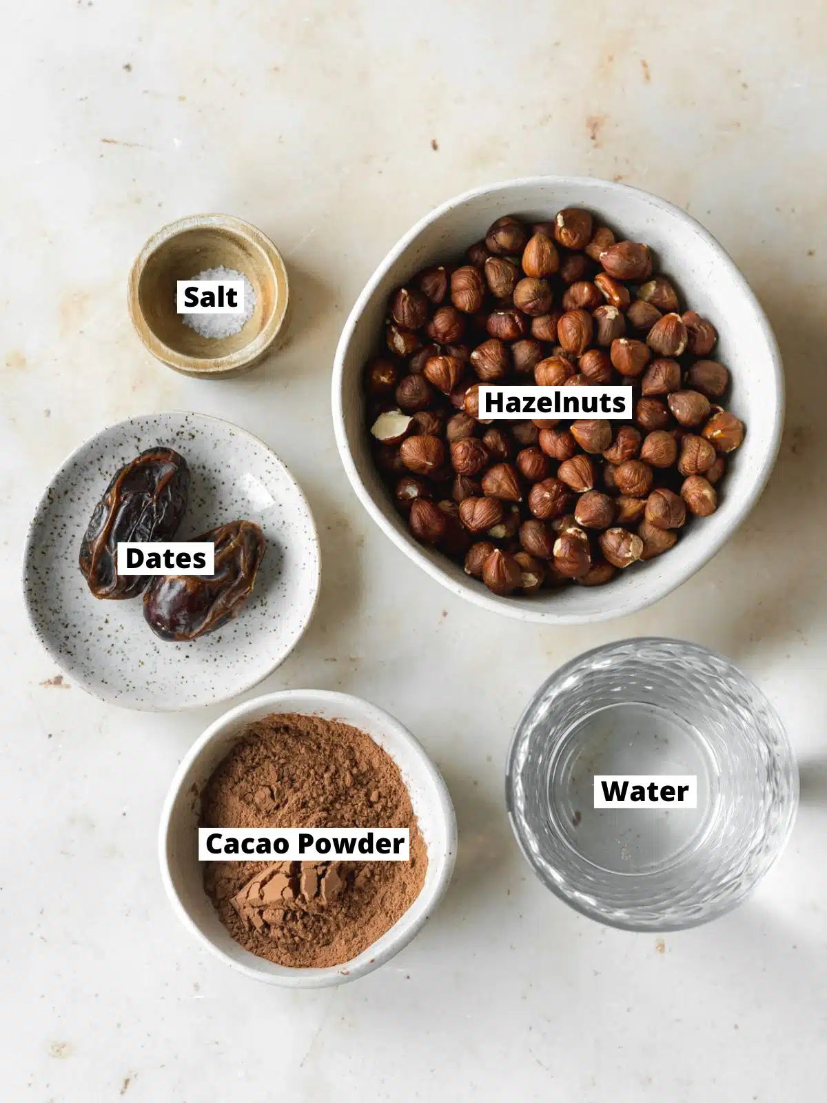 ingredients for hazelnut milk measured out in bowls on a marble surface.