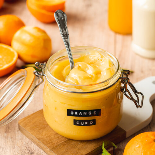 a jar of orange curd with peeled oranges scattered around it.